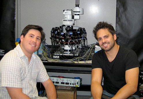 Joint first authors of the paper Rodrigo Perin (on the left) and Costas Anastassiou (on the right) in front of the electrophysiological instrument used for the experiments.
